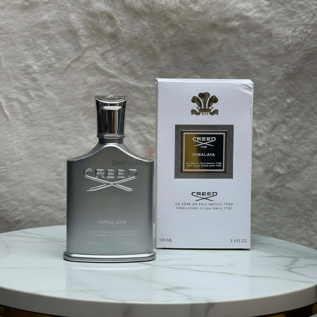 Creed Himalaya perfume bottle and packaging on a textured surface with flowers in the background.